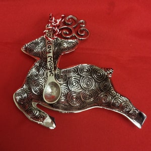 May include: Silver reindeer shaped dish with a spoon that says "Holiday Magic" on it. The reindeer has a swirl pattern and a red and white ribbon on its head.