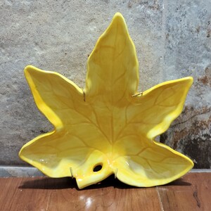 May include: A yellow ceramic leaf-shaped dish with a hole in the centre. The dish has a glossy finish and is decorated with raised veins.