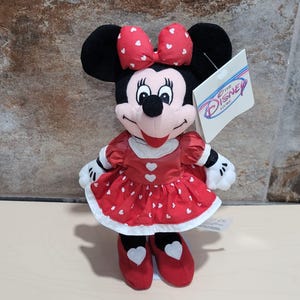 K&ouml;nnte beinhalten: Ein Minnie Mouse Pl&uuml;schtier. Die Puppe hat ein rotes Kleid mit wei&szlig;en Herzakzenten, eine passende Schleife und rote Schuhe. Das Disney Store-Etikett ist angebracht. Das Pl&uuml;schtier ist schwarz, wei&szlig; und rot.