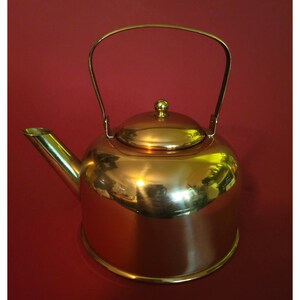 Puede incluir: Una tetera de cobre con asa y tapa de latón. La tetera tiene un acabado brillante y pulido.