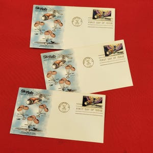 May include: Three white envelopes featuring Skylab First Day of Issue commemorative stamps and postmarks from Houston, Texas, dated 14 May 1974. The envelopes display illustrations of the Skylab space station and mission crew names in blue and orange.