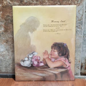 Könnte beinhalten: Ein gerahmter Druck, der ein junges Mädchen beim Beten zeigt, mit zwei Stofftieren daneben. Das Kunstwerk enthält eine Silhouette und den Text "Mommy Said" mit einem Gedicht.