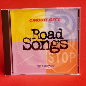 May include: A CD sampler for "Road Songs" from Circuit City. The CD cover features a colorful design with road signs, a speedometer, and the text "Road Songs" in large, bold letters.