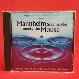Könnte beinhalten: Eine CD-Hülle mit dem Album "Mannheim Steamroller Meets the Mouse". Das Cover zeigt ein blaues und violettes Wassertropfen-Design. Der Text enthält "Walt Disney Records" und "Unique Musical Creations Based on Disney Songs."