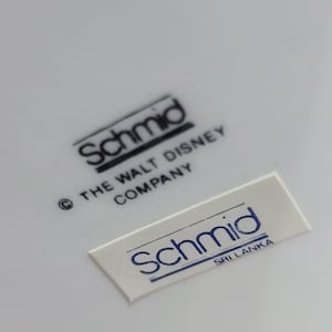 Puede incluir: Primer plano de un plato de cer&aacute;mica blanco con dos etiquetas en blanco y negro. La etiqueta superior dice "Schmid &copy; THE WALT DISNEY COMPANY". La etiqueta inferior dice "Schmid SRI LANKA".
