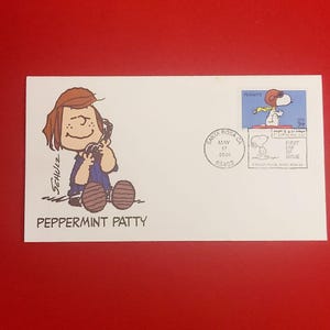 Op de afbeelding: Witte envelop met een Peanuts-cartoon van Peppermint Patty en een Snoopy-postzegel. De envelop is gestempeld met "Santa Rosa CA" en de datum "17 mei 2001". De postzegel luidt "USA 34".