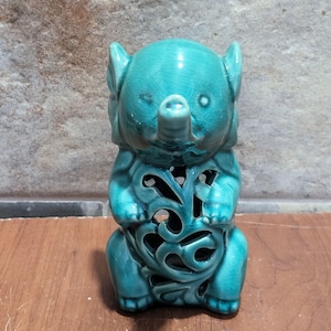 May include: A teal blue ceramic elephant figurine with a decorative cutout design. The elephant is standing on all four legs and has a curled trunk.