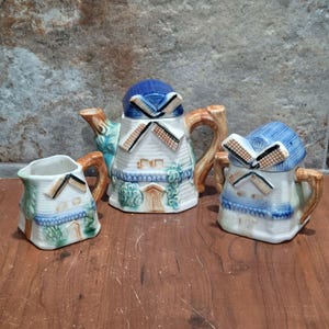 Può includere: Un set da tè in ceramica vintage con un design a mulino a vento. La teiera, la brocca per la panna e lo zuccheriera sono tutti decorati con vernice blu, bianca e verde. Le pale del mulino a vento sono marroni e bianche.