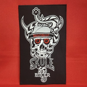 Può includere: Toppa ricamata in bianco e nero con un teschio che indossa un cappello con la scritta "Easyriders" e un serpente avvolto attorno ad esso. Il testo "Skull Biker" è sotto il teschio.