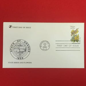 以下が含まれることがあります： オレゴン州の紋章、「STATE BIRDS AND FLOWERS」の文字、ニシマキバドリとオレゴンブドウが描かれた20セント切手が貼られた白い初日カバー。1982年4月14日にワシントンDCで消印が押されている。