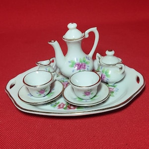 May include: A white porcelain tea set with floral designs. The set includes a teapot, creamer, sugar bowl, and two teacups and saucers. The set is on a white tray with a gold rim.