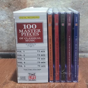 May include: A boxed set of five CDs titled "100 Masterpieces of Classical Music" by Time Life Music. The box is white with red and gold text. Each CD case is a different colour: orange, red, green, purple, and blue. Each CD is labelled with a volume number.