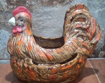 Peut inclure: Un pot en céramique en forme de coq, aux couleurs marron, orange et rouge. Le pot présente un design détaillé, avec une crête et des barbillons rouges, et une queue incurvée. Il est conçu pour contenir des plantes ou d'autres objets décoratifs.