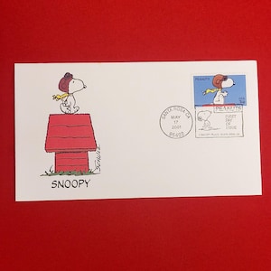 Könnte beinhalten: Ein weißer Umschlag mit einer Snoopy-Illustration. Snoopy ist auf seinem roten Hundehäuschen abgebildet, darunter das Wort "SNOOPY". Ein Stempel und ein Poststempel aus Santa Rosa, CA, sind ebenfalls zu sehen.