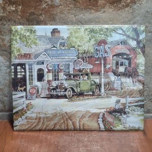 Könnte beinhalten: Ein Vintage-Druck, der eine ländliche Szene mit einer Garage, einer Tankstelle und einer überdachten Brücke zeigt. Ein grüner Oldtimer parkt vor der Garage. Der Druck enthält den Text "Garage Blacksmith" und "Gas".