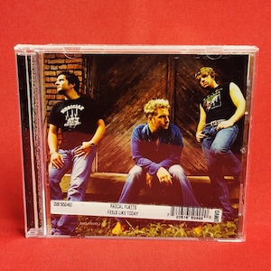 May include: A Rascal Flatts CD case featuring three men in casual attire. The album cover shows the band members in front of a wooden door. The album title "Feels Like Today" is printed on the bottom.