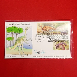 Könnte beinhalten: Ein Gedenkumschlag mit Dinosaurierillustrationen und Briefmarken. Der Umschlag enthält den Text "THE WORLD OF DINOSAURS" und "FIRST DAY OF ISSUE". Die Briefmarken zeigen Corythosaurus, Ornithomimus und Parasaurolophus.