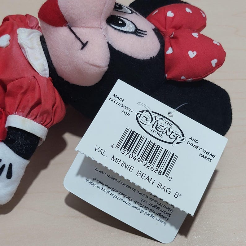 K&ouml;nnte beinhalten: Minnie Mouse Bean Bag Pl&uuml;schtier mit roter Schleife mit wei&szlig;en Herzen. Auf dem Etikett steht "VAL. MINNIE BEAN BAG 8" und "The Disney Store". Das Pl&uuml;schtier ist schwarz, rot und wei&szlig;.