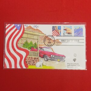May include: A red, white, and blue American flag is draped over a porch with a red car parked in front. The car has a white cat sitting next to it. The image is a first day of issue stamp from San Antonio, Texas, dated June 15, 1996.