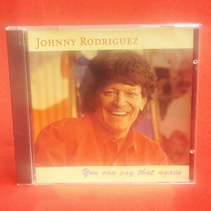 Może przedstawiać: Pudełko na CD z Johnnym Rodriguezem. Tekst "Johnny Rodriguez" znajduje się na górze, a "You can say that again" na dole. Okładka przedstawia uśmiechniętego mężczyznę w pomarańczowej koszuli.