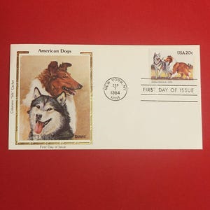 以下が含まれることがあります： 犬のイラストが描かれた初日発行の封筒。メイン画像はコリーとシベリアンハスキー。切手にはアラスカンマラミュートとコリーが描かれています。「American Dogs」と「First Day of Issue」の文字が含まれています。