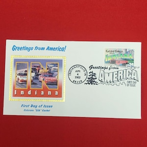以下が含まれることがあります： Greetings from Americaをテーマにした白い初日カバー。インディアナ州の切手、2002年4月4日のインディアナポリスの消印、レースカーが描かれた金色の縁取りのキャッシュが印刷されており、IN Indianaという文字が含まれています。