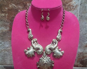 Conjunto de collar y pendientes Lucia en tono dorado con diseño floral ornamentado.