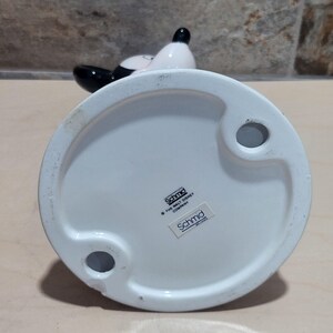 Puede incluir: Figura de cer&aacute;mica blanca de un perro blanco y negro con un lazo rojo. La figura est&aacute; hecha por Schmid y tiene licencia de The Walt Disney Company.