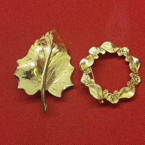 May include: Two gold-toned brooches. One is a leaf design and the other is a circle with a floral design.