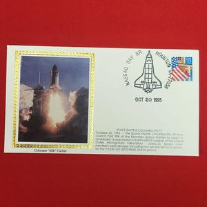 May include: A white commemorative envelope featuring a Colorano Silk Cachet of the Space Shuttle Columbia launch. It includes a Nassau Bay, TX postmark dated Oct 20 1995, a 32-cent USA flag stamp, and printed text detailing the STS-73 mission launch.