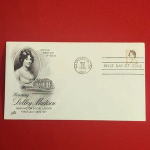 以下が含まれることがあります： ドリー・マディソン夫人の肖像画が描かれた白い封筒で、「Honoring Dolley Madison」の文字が入っています。「初日発行」の切手と、1980年5月20日のワシントンD.C.の消印が含まれています。