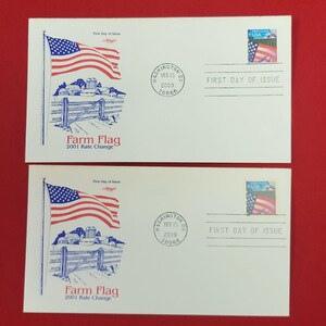 以下が含まれることがあります： 農場とたなびくアメリカ国旗の青いインクのイラストが描かれた2枚の白い封筒。各封筒には切手、2000年12月15日のワシントンDCの消印、Farm Flag 2001 Rate ChangeおよびFirst Day of Issueという文字が印刷されています。