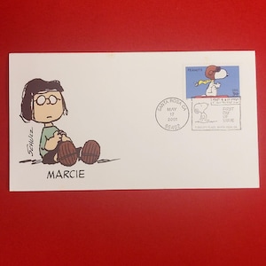 May include: A white envelope featuring a cartoon illustration of Marcie from Peanuts, with the name "MARCIE" below. A "First Day of Issue" stamp with Snoopy is on the right, and a Santa Rosa, CA postmark is in the center. The envelope is on a red background.