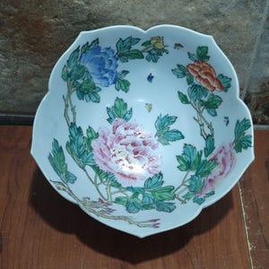 May include: A white porcelain bowl with a scalloped rim and a floral design. The bowl is decorated with pink, blue, and orange flowers, green leaves, and butterflies.