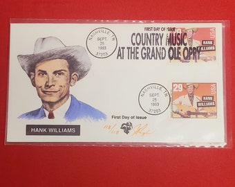 May include: A first day of issue envelope featuring a portrait of Hank Williams, a country music legend. The envelope is white with blue and red accents. The envelope has a stamp with a picture of Hank Williams playing a guitar. The envelope also has a stamp with the text "COUNTRY MUSIC AT THE GRAND OLE OPRY".
