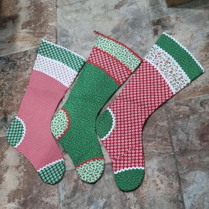 May include: Three Christmas stockings in red, green, and white patterns. The stockings have a traditional design with a rounded heel and toe, and a scalloped trim. The fabrics feature polka dots and floral prints.