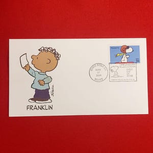 May include: A white envelope featuring a cartoon illustration of Franklin from Peanuts, holding a paper. The envelope has a stamp with Snoopy and the text "Peanuts". Includes a postmark from Santa Rosa, CA, dated May 17, 2001.