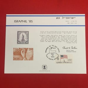 Puede incluir: Un sobre conmemorativo ISRAPHIL '85 con sellos que representan la Estatua de la Libertad y una persona. El sobre incluye texto en hebreo e inglés, junto con un sello del Servicio Postal de EE. UU. y la bandera estadounidense.