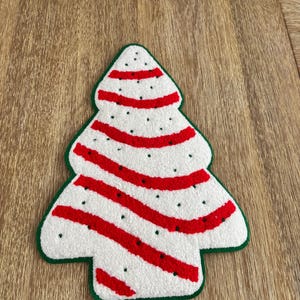 May include: A Christmas tree-shaped rug with a white base, red stripes, and small black dots. The tree is outlined in green. This festive rug is perfect for holiday decor.