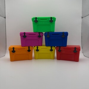May include: A stack of seven small, colorful coolers. The coolers are in shades of green, pink, blue, orange, yellow, and red. Each cooler has a black handle and the word "YETI" printed on the front.
