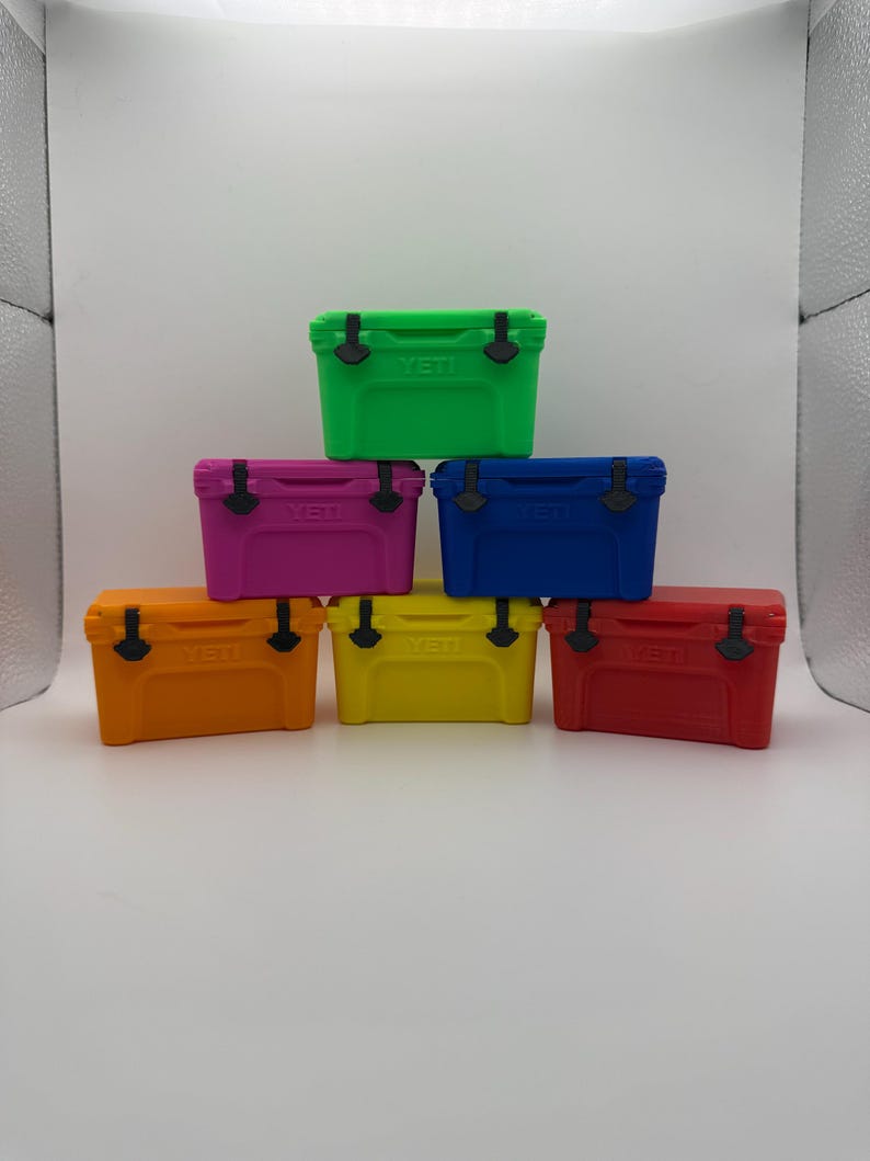 May include: A stack of seven small, colorful coolers. The coolers are in shades of green, pink, blue, orange, yellow, and red. Each cooler has a black handle and the word "YETI" printed on the front.