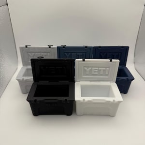 May include: A collection of small, hard-sided coolers in various colors, including white, black, and blue. Each cooler has a hinged lid and the brand name "YETI" is visible on the front. The coolers are designed to keep items cold.