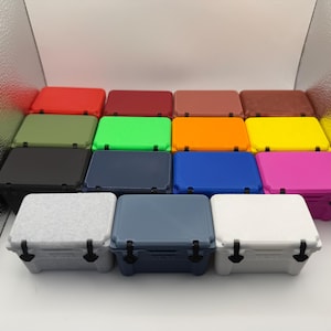 May include: A collection of small, colorful coolers in various shades, including red, green, blue, and pink. Each cooler has a rectangular shape with a matching lid and black latches, perfect for outdoor activities.