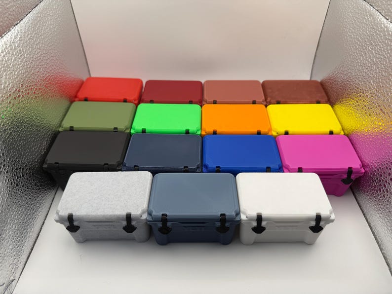 May include: A collection of small, colorful coolers in various shades, including red, green, blue, and pink. Each cooler has a rectangular shape with a matching lid and black latches, perfect for outdoor activities.