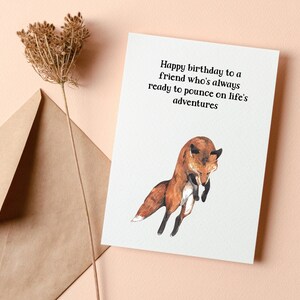 May include: A white card with a brown fox jumping in the air. The card has the text "Happy birthday to a friend who's always ready to pounce on life's adventures".