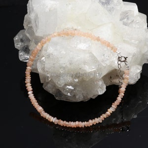 May include: A delicate pink sunstone beaded bracelet with a silver clasp. The bracelet is displayed on a bed of white crystals.