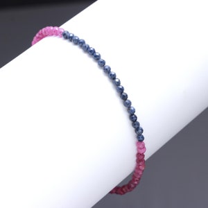 Puede incluir: Un delicado brazalete hecho con pequeñas piedras preciosas azules y rosas facetadas. El brazalete está enhebrado en un cordón elástico transparente y mide aproximadamente 18 cm de largo.