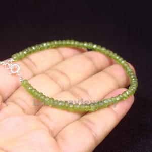 以下が含まれることがあります： 小さな、ファセット加工されたオリーブグリーンのビーズが特徴の繊細なブレスレット。ブレスレットはシルバーチェーンに通され、小さな丸い留め金で留められています。ビーズは均一なサイズと形状で、均一な外観を作り出しています。