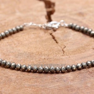 Könnte beinhalten: Ein silbernes Armband mit einer Kette und einer Reihe kleiner, facettierter, grauer Pyritperlen.