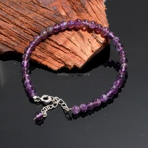 Könnte beinhalten: Ein Armband aus violetten Amethyst-Edelsteinen mit einem silbernen Verschluss und einer Verlängerungskette. Das Armband besteht aus runden Perlen und ist etwa 18 cm lang.